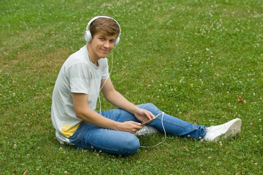 young man relaxing with a tablet pc listening music with headphones at the park, outdoor