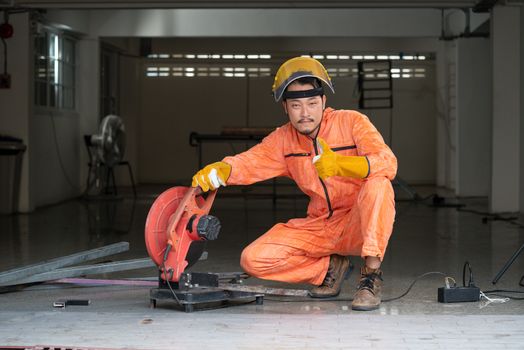 The steelworker poses confidently at his work site. Metal grinding on steel spare part in workshop. Industrial worker cutting and welding metal.