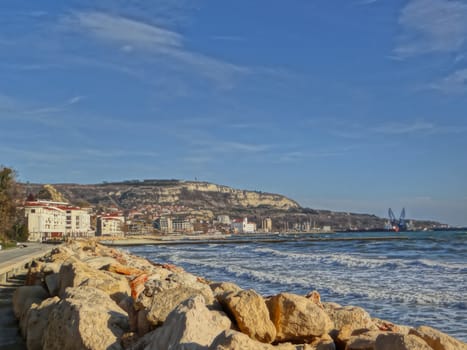 Seacoast landscape with some buildings and a hill for background.