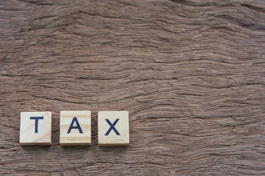 Tax with wooden alphabet blocks, on plank wooden background with copy space

