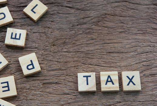 Tax with wooden alphabet blocks, on plank wooden background with copy space
