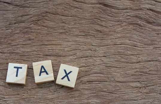 Tax with wooden alphabet blocks, on plank wooden background with copy space
