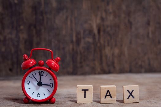 Tax with wooden alphabet blocks and Red alarm clock, on Table dark plank wooden background with copy space
