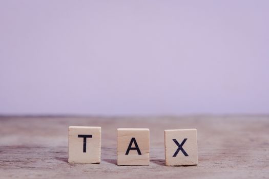 Tax with wooden alphabet blocks, on plank wooden background with copy space
