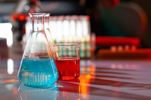 Illuminated laboratory flask filed with colorful chemical solutions with shadows on the table. Laboratory, science, reaserch, chemistry... consept.