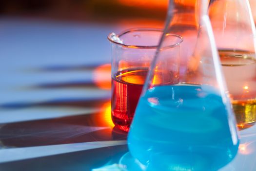 Illuminated laboratory flask filed with colorful chemical solutions with shadows on the table. Laboratory, science, reaserch, chemistry... consept.