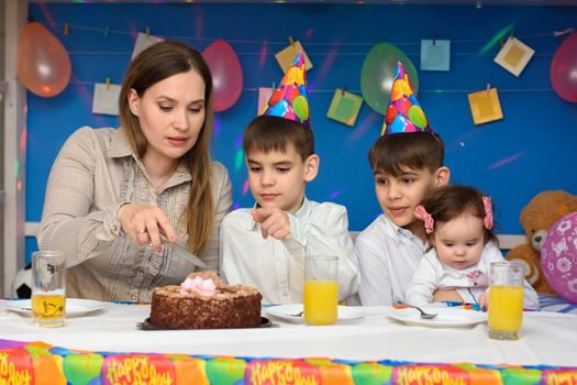 Mom cuts a birthday cake with her children