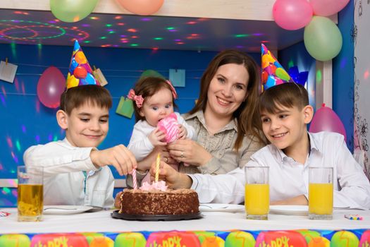 Children on a family birthday put candles in a birthday cake