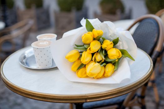 Yellow tulips bouquet with coffee cups over wooden table