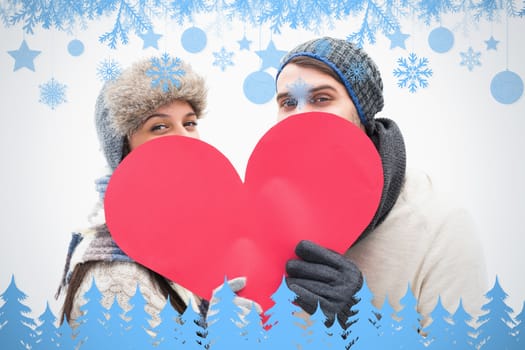 Attractive young couple in warm clothes holding red heart against snow flake frame in blue