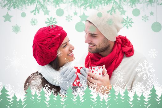 Attractive young couple in warm clothes holding mugs against snowflakes and fir trees in green