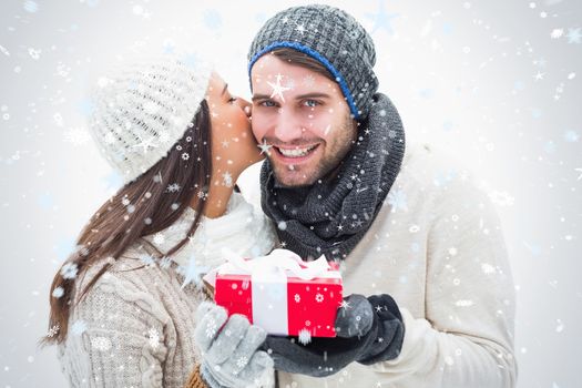 Attractive young couple in warm clothes holding gift against snow falling