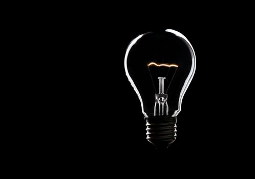 Burning light bulb on black background. Symbol for bright ideas with copy space