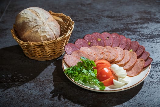 Slicing different types of sausages on a plate with herbs and vegetables on a gray background