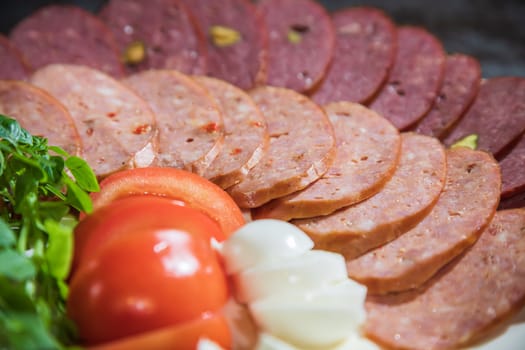 Slicing different types of sausages on a plate with herbs and vegetables on a gray background