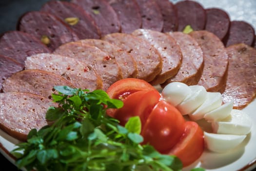Slicing different types of sausages on a plate with herbs and vegetables on a gray background