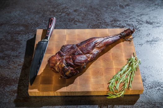 Smoked lamb leg on a wooden board with a knife and rosemary