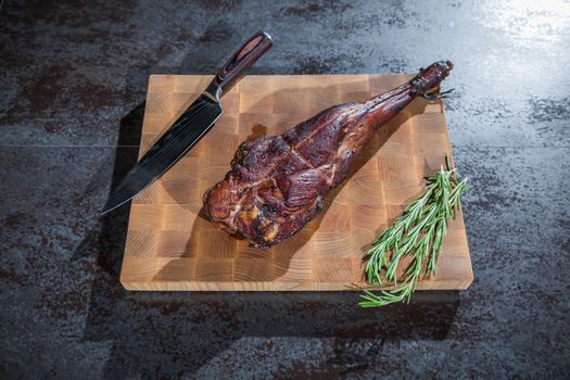 Smoked lamb leg on a wooden board with a knife and rosemary