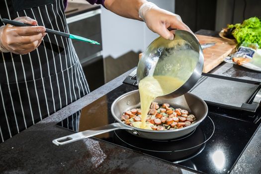 Cook cook an omelet with onions and sausages in a pan