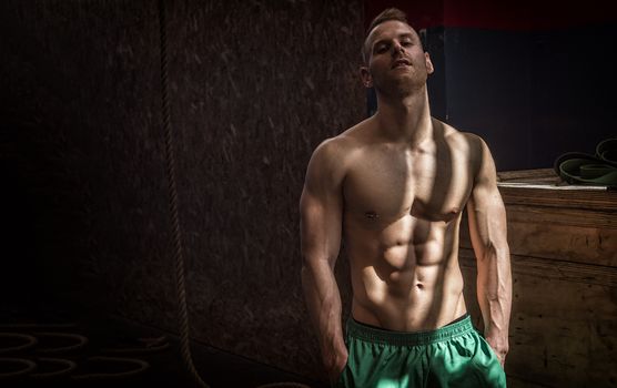 Handsome muscular young man standing in gym during workout, looking at camera