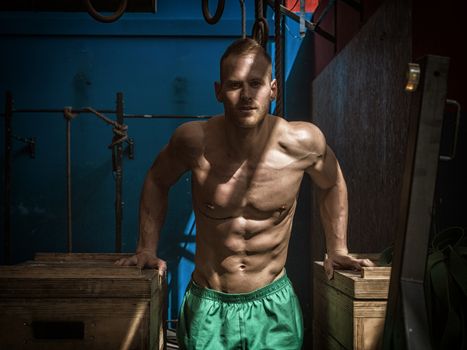 Handsome muscular young man standing in gym during workout, looking at camera