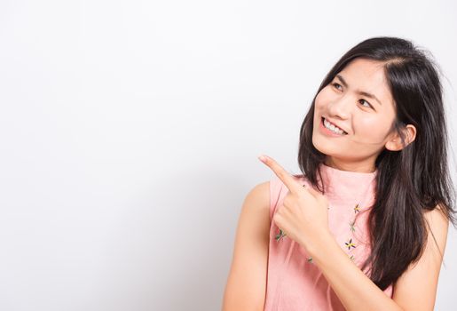 Portrait Asian beautiful young woman standing smile seeing white teeth, She pointing finger up and looking at side, shoot photo in studio on white background. There was copy space to put text