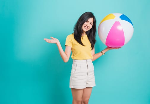 Happy Asian young beautiful woman smiling white teeth standing wear shirt her holding beach ball in summer holiday travel isolated studio shot on blue background with copy space for text