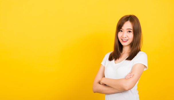 Asian happy portrait beautiful cute young woman teen standing wear t-shirt smile her confidence with crossed arms looking to camera isolated, studio shot on yellow background with banner copy space