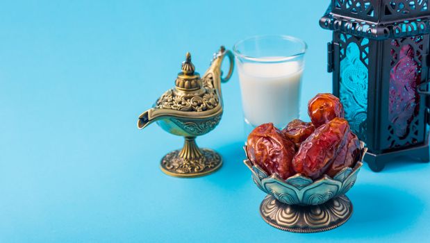 Ramadan Kareem fasting Food Concept, Bronze plate dates, milk, and lantern Aladdin lamp decoration, eid Arabian Muslim religious festival on a blue background with copy space for text