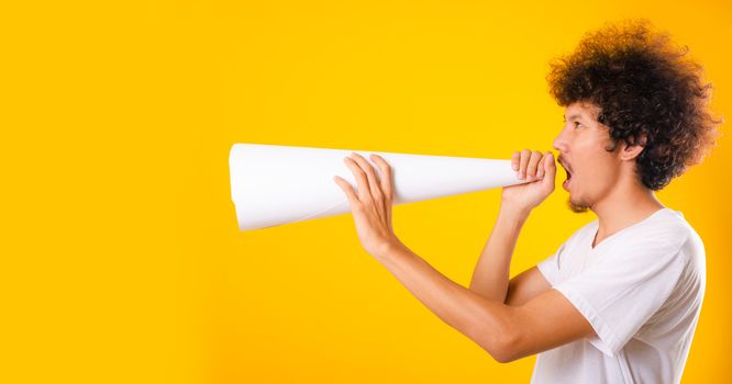 Asian handsome man with curly hair he announcing or spreading news using white speaker paper isolate on yellow background