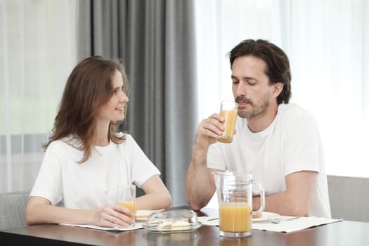 Happy, attractive mid adult couple eats breakfast together at home, orange juice