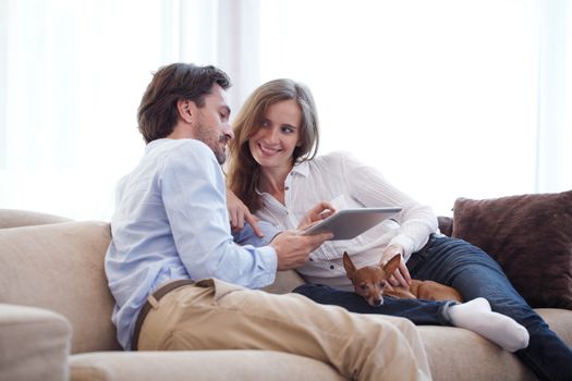 Couple at home with pet dog looking at digital tablet