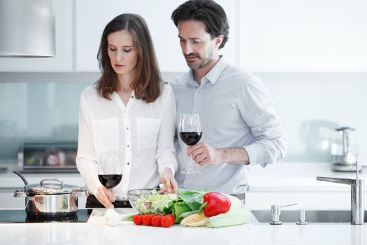 Couple drinking red wine in kitchen and cooking healthy dinner together