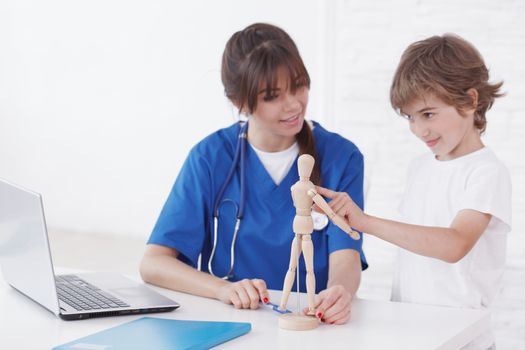 Boy at doctor office, young medical worker general practitioner pediatrician explain medicine uding wooden doll