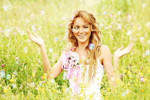 Blonde girl starts soap bubbles and smiling in a green spring field