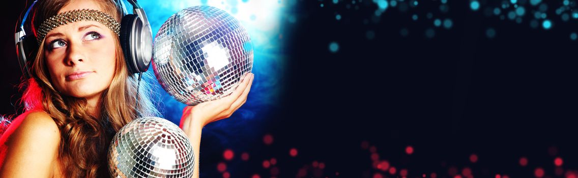 Disco girl enjoys music in head phones holding mirror disco ball over black and colorful bokeh background