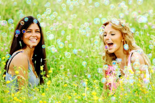 Happy smling girlfriends on green grass field in soap bubbles