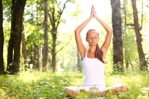 Yoga woman in white on green park grass in lotus asana pose