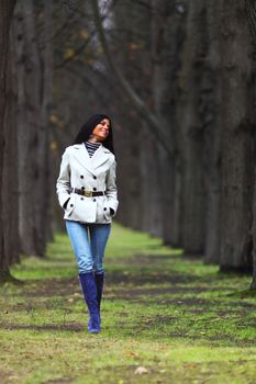 Happy smiling young woman walk in autumn park with bare trees