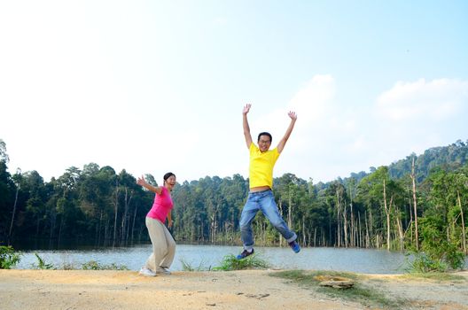 Asian couple jumping with joy by a lake