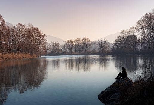Silhouette of a person sitting on the edge of the river at sunset, Italian landscape