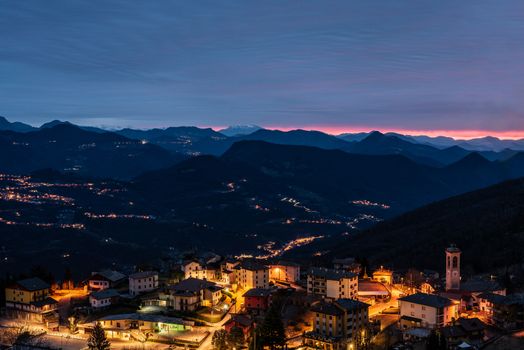 The sun rises over a small mountain village still illuminated by night lights