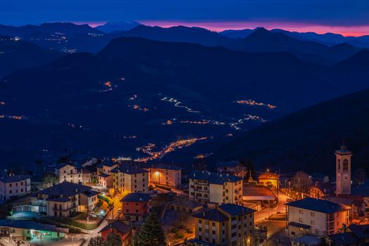 The sun rises over a small mountain village still illuminated by night lights