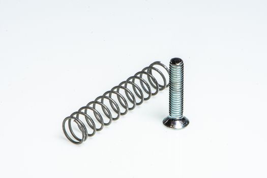 Detail of a small metal spring next to a small steel screw on a white background