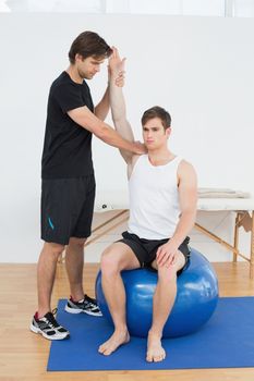 Young man sitting on yoga ball while working with a physical therapist