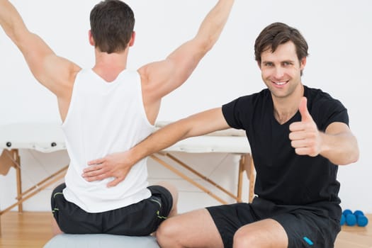 Physical therapist gesturing thumbs up besides man on yoga ball