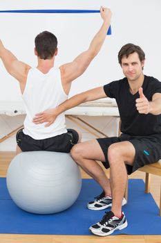 Physical therapist gesturing thumbs up besides man on yoga ball