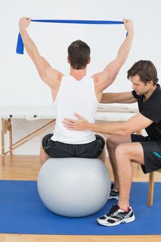 Young man sitting on yoga ball while working with a physical therapist