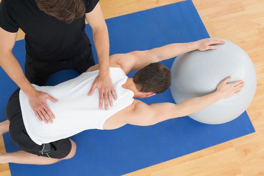 High angle view of a physical therapist assisting young man with yoga ball in the gym at hospital