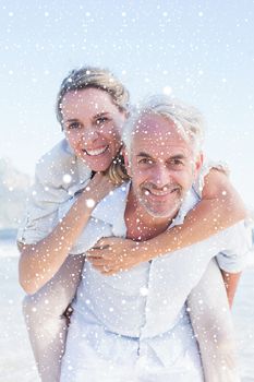 Man giving his smiling wife a piggy back at the beach against snow falling